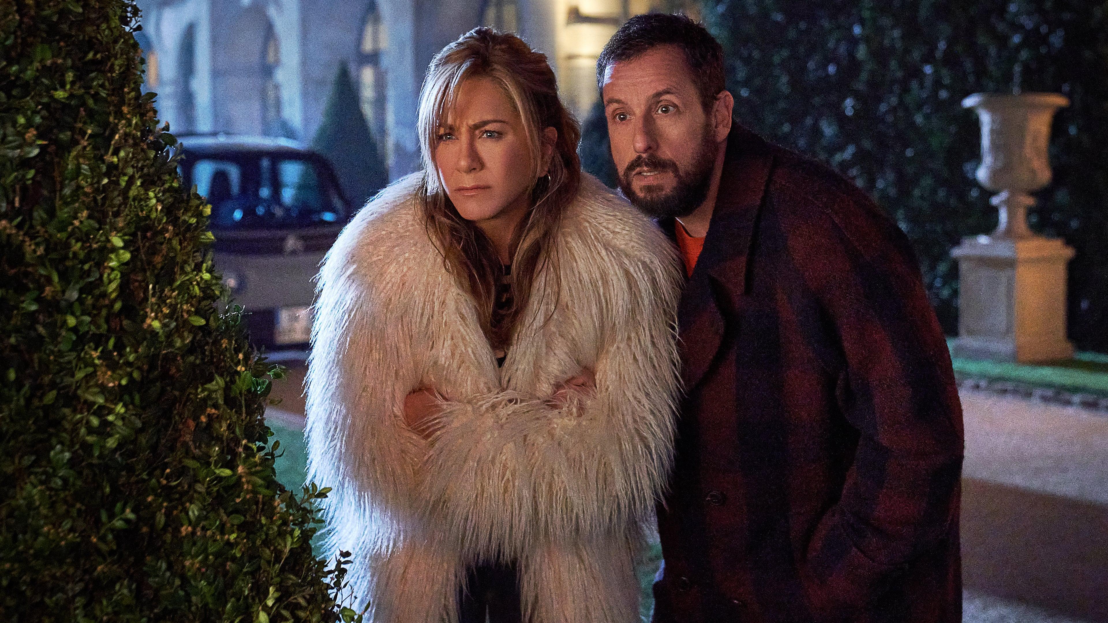 Jennifer Aniston wears a fuzzy coat as she stands to the left of Adam Sandler in this still from Netflix's 'Murder Mystery 2.'